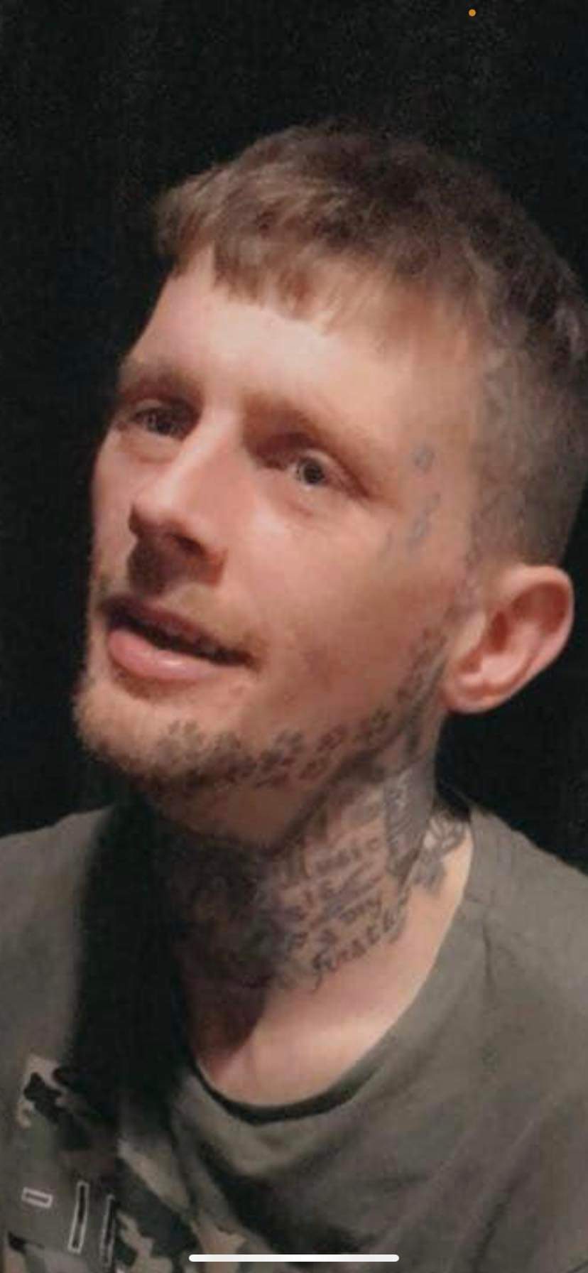 A white man with short dark blonde hair and tattoos on his face and neck looking off camera