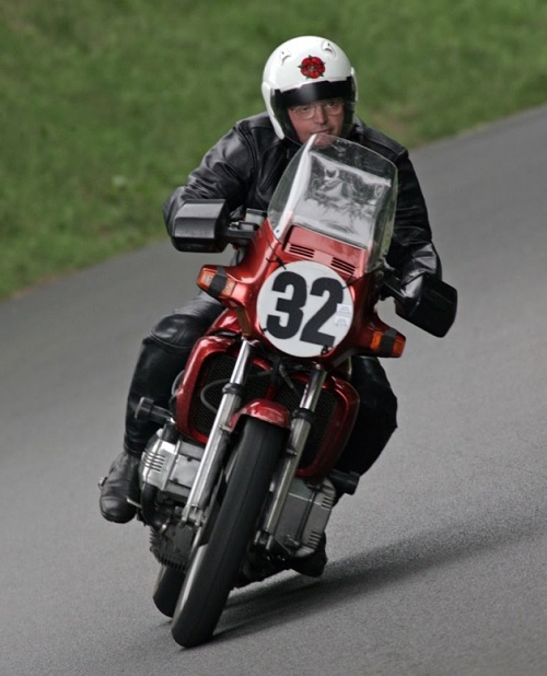 Man with white helmet riding red motorbike along road