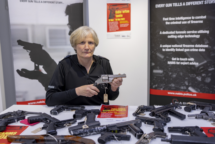 Light-haired woman sat around table of guns