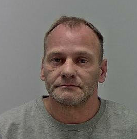 49 year old man with dark hair, receding hairline, short stubble, wearing a grey sweatshirt