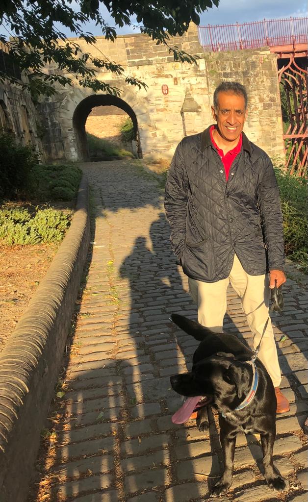 Smiling Asian man wearing red-shirt and grey jacket, with black Labrador dog