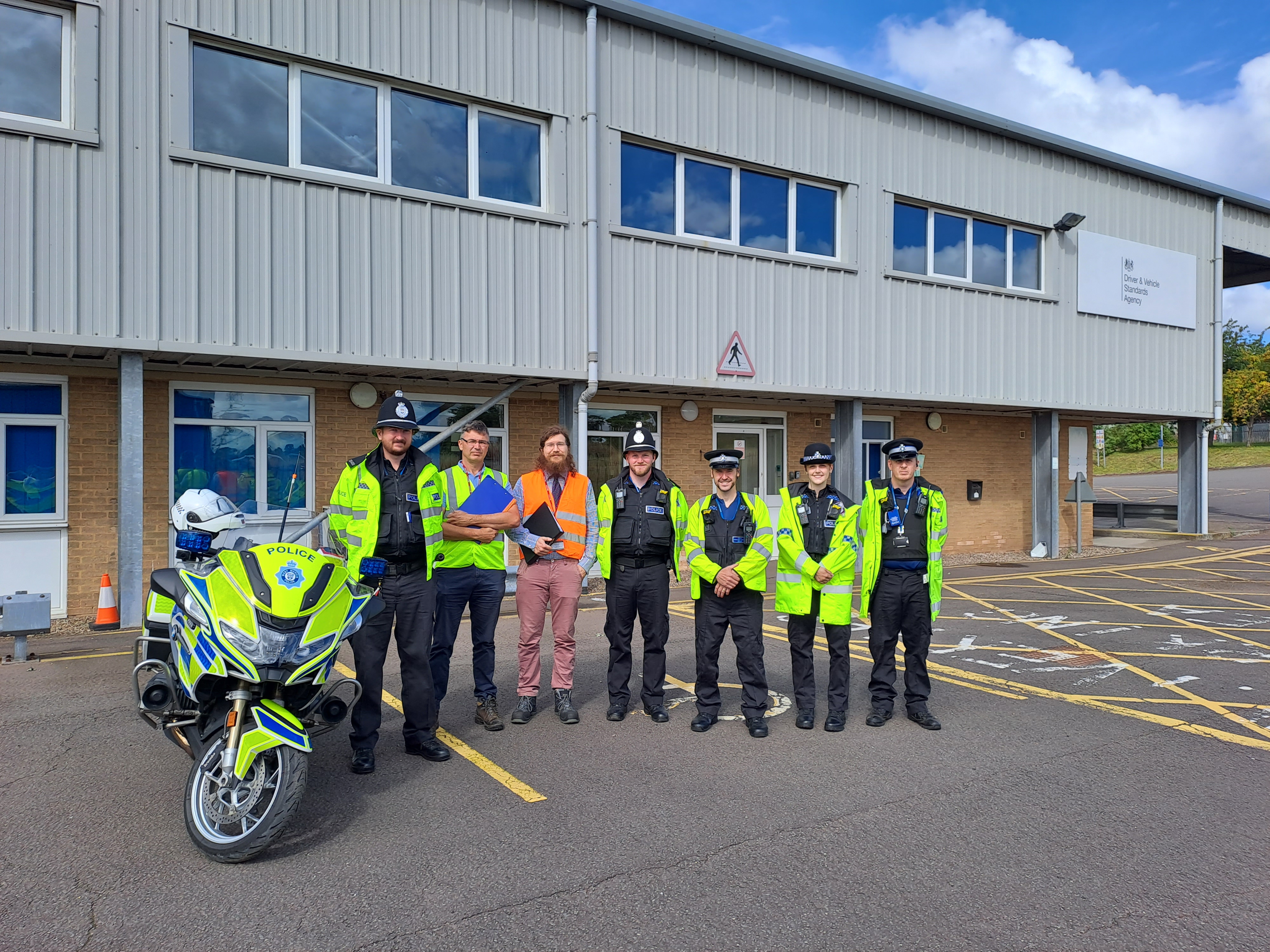 A group of police officers stood by a police motorbike outside a building