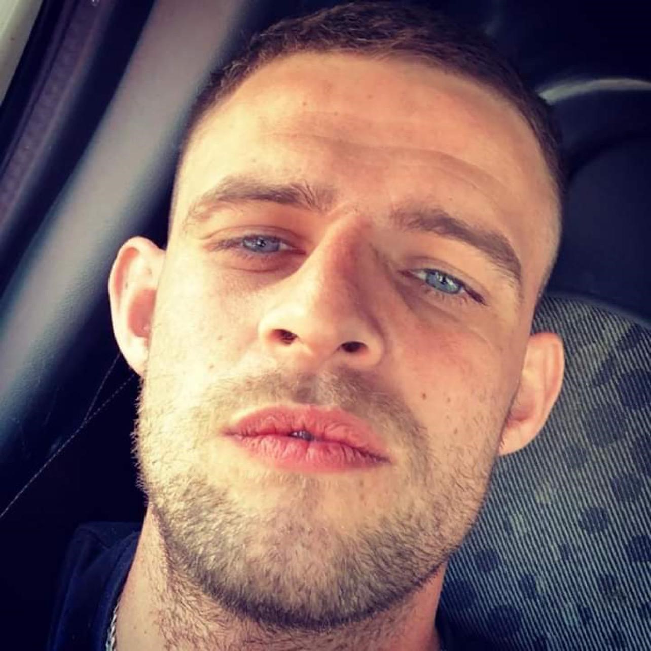 Picture of a white man, blue eyes and dark features looking at the camera 