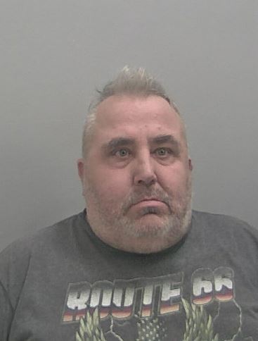 A heavy set man with short grey hair and a stubbly grey beard
