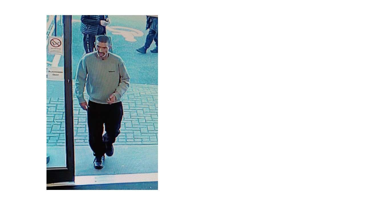 CCTV image of white man walking into the shop. Grey jumper