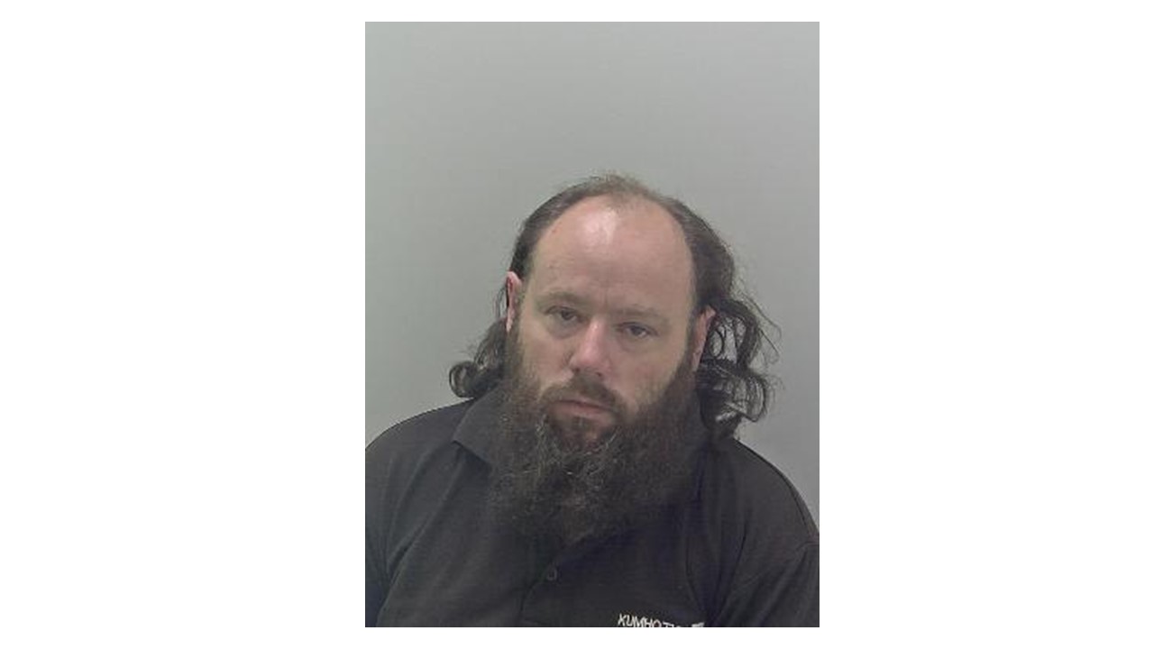 White man, balding head with long dark at the back. Long beard and black top