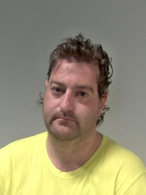 A man wearing a yellow shirt. He has curly hair and moustache.