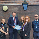 A group of people standing outside a police station smiling looking at the camera. 