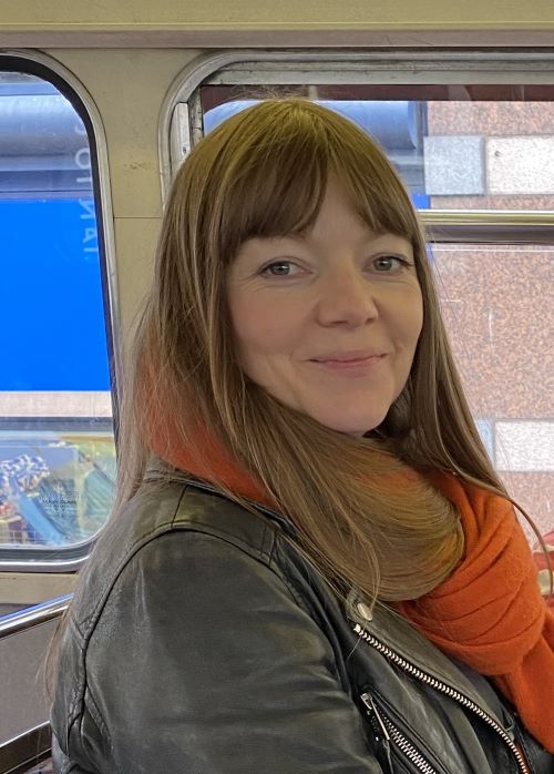 White female with long brown hair, smiling at the camera.