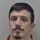 A custody picture of man wearing a pink plaid shirt over a white t-shirt. He has black hair and moustache.