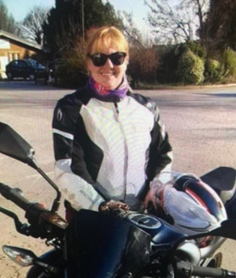 Woman in leathers with a motorbike, wearing sunglasses.