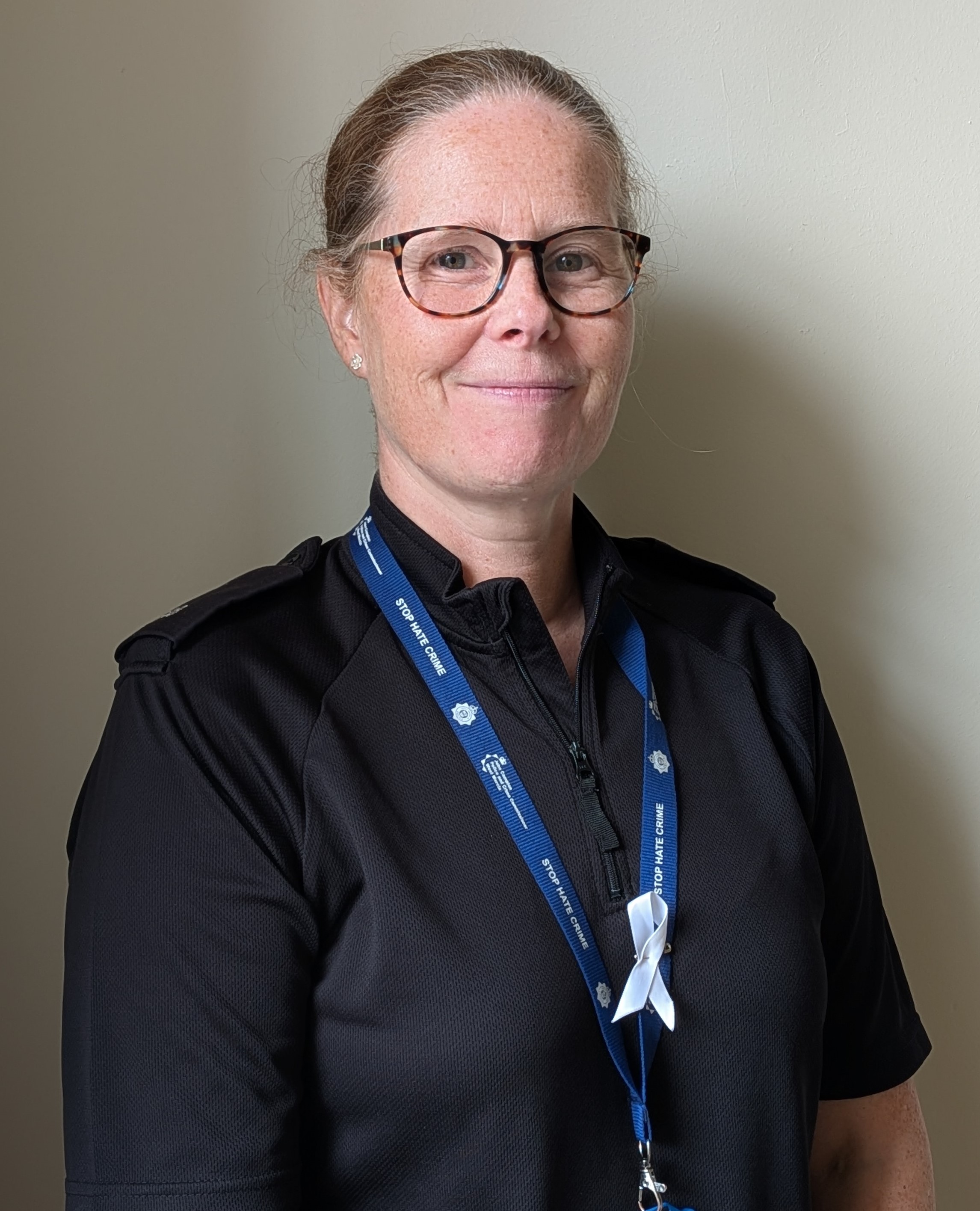 White female police officer, wearing glasses and smiling.