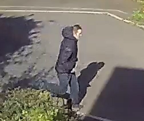 White man, wearing dark jacket, walking along a street