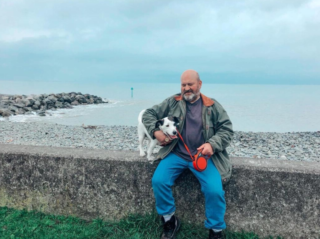 man sat on wall by beach with dog on his lap