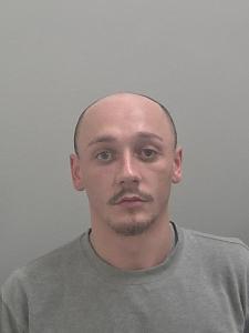 White male, bald and wearing a grey jumper. 