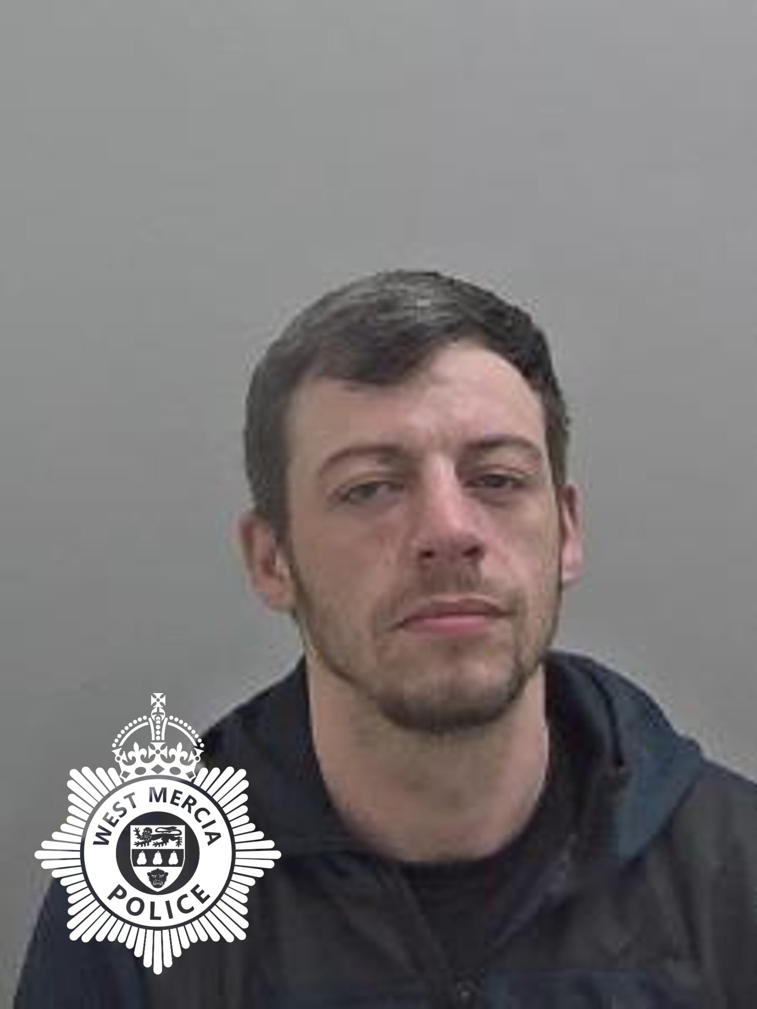 A mugshot of a man with short dark hair and a light beard, with the West Mercia Police logo in the bottom left corner.