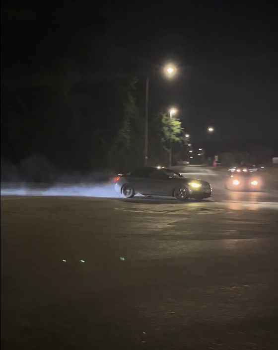 A blue car doing driving dangerously on a public road at night