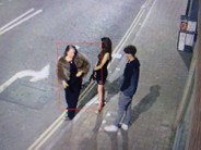 Two women and a man stood on a street.