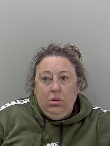 White female, brown hair tied up and wearing a green jacket.