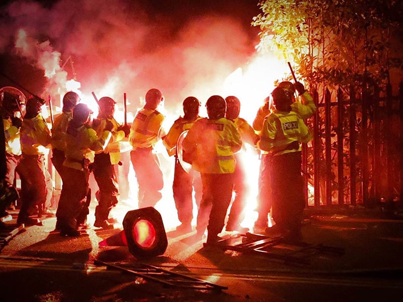 police officers in public order uniform in front of big cloud of red flare smoke