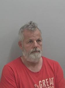 White male, with white hair and beard, wearing a red t shirt. 