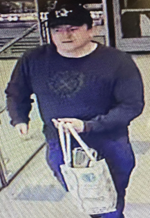 White male wearing cap and blue jumper, holding bag. 